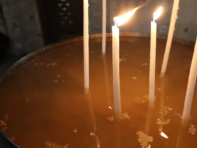 נרות לבנים דקים דולקים, ניצבים בתוך אגן מים חומים.