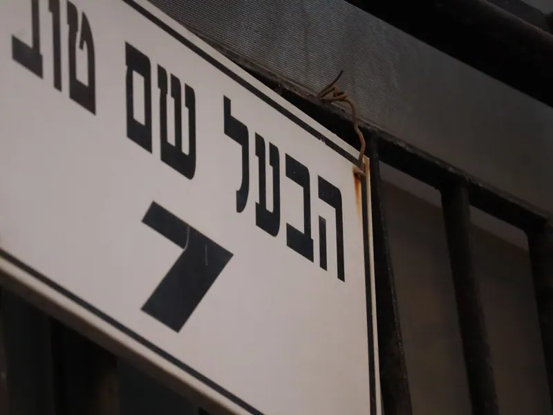 שלט לבן בכתב עברי שחור: "הבעל שם טוב", בצילום מקרוב ובזווית.