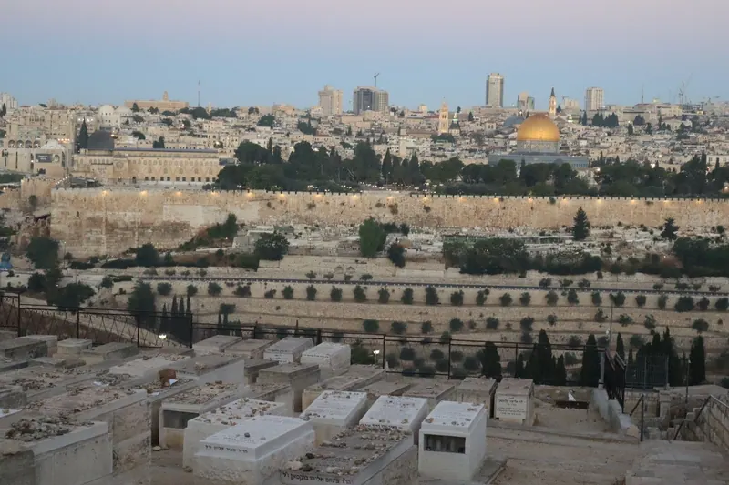 קברים לבנים בבית הקברות היהודי בהר הזיתים, ומעבר לעמק חומת העיר העתיקה וכיפת הסלע באור הערב.
