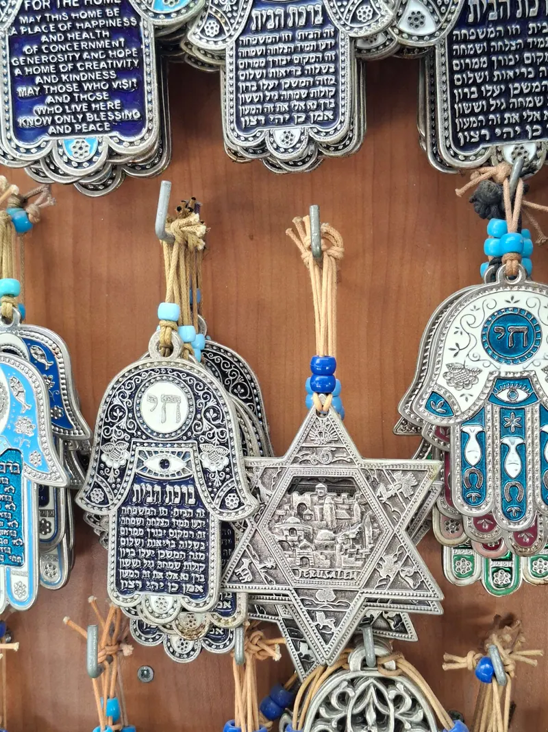 חמסות מתכת עם "ברכת הבית", "חי" ועין כחולה, ומגן דוד עם תבליט של ירושלים, תלויים על לוח עץ.