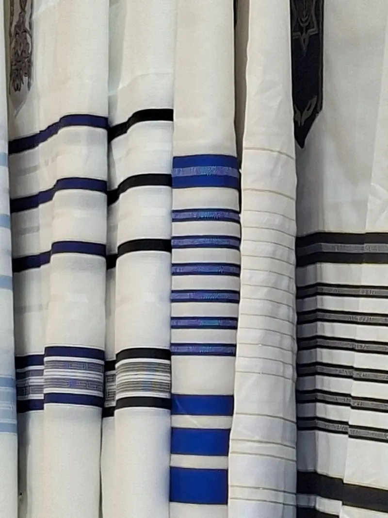 טליתות לבנות תלויות זו לצד זו, עם פסים כחולים ושחורים ועטרות רקומות.