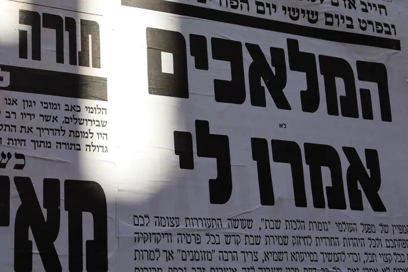 מודעות קיר בעברית באותיות שחורות גדולות, ובהן הכותרת "המלאכים אמרו לי", באור שמש ובצל.