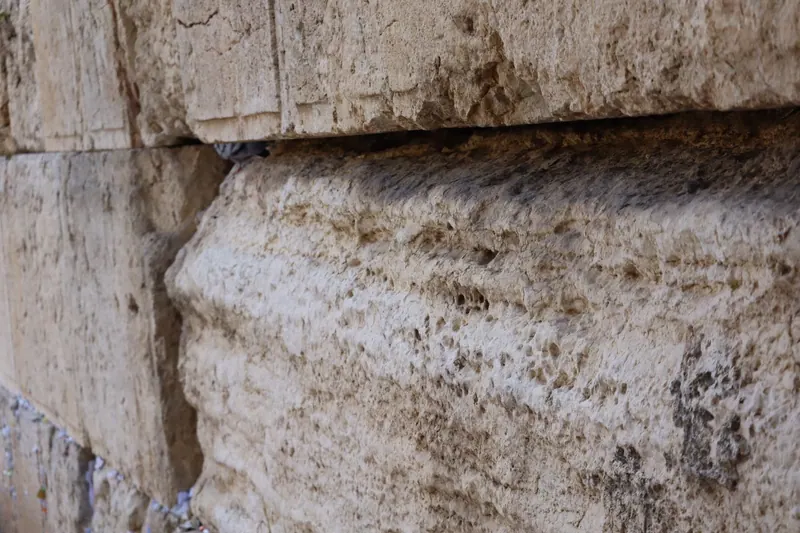אבני הכותל הגדולות מקרוב, שחוקות ומחוררות, ופתקים תחובים בסדקים שבתחתית.
