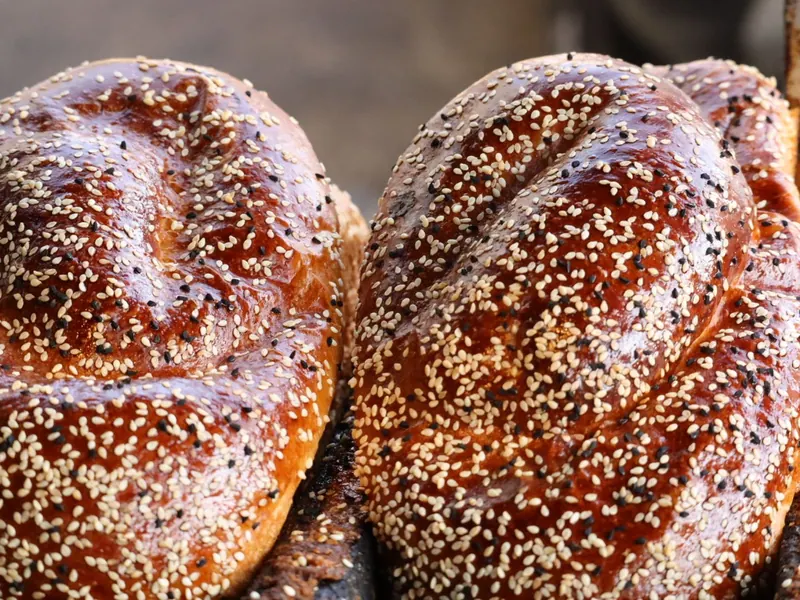 שתי חלות קלועות מבריקות זרועות שומשום לבן ושחור, בצילום מקרוב.