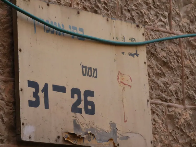 שלט ישן ודהוי על קיר אבן: "ממס' 26–31", וכבל ירוק חוצה אותו.