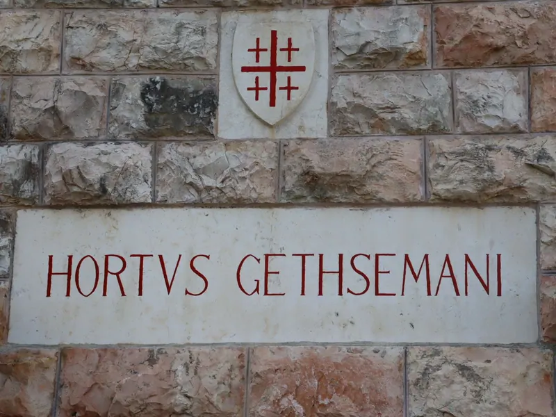 שלט אבן עם הכיתוב HORTVS GETHSEMANI באותיות אדומות, ומעליו מגן ועליו צלב ירושלים.