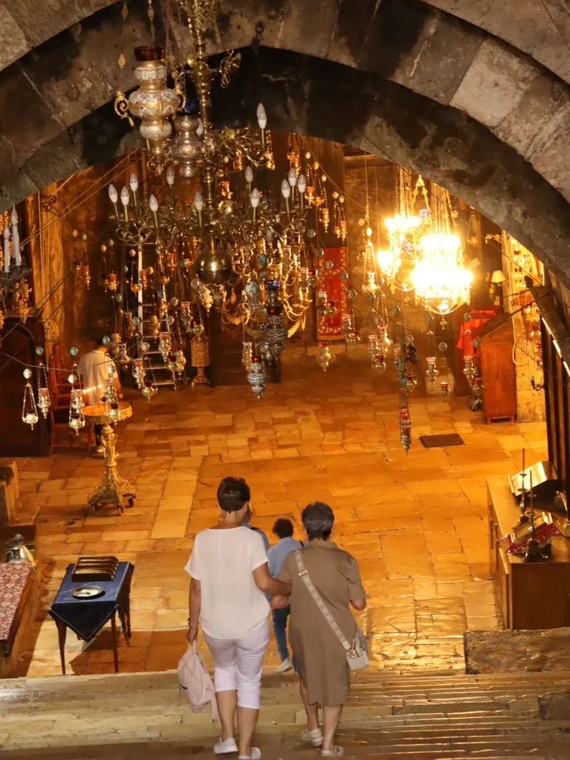 מדרגות אבן רחבות יורדות אל חלל כנסייה המואר במנורות תלויות; שני מבקרים יורדים בהן, מצולמים מאחור.