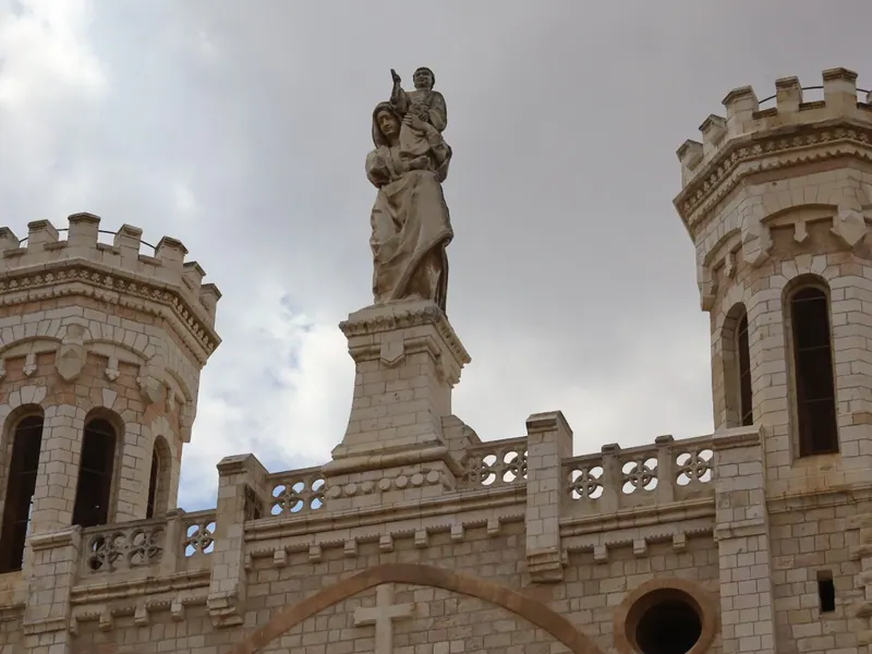 פסל מריה והתינוק ניצב בין שני מגדלים משוננים בראש מבנה נוטרדאם, במבט מלמטה.