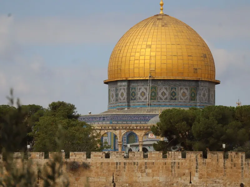 כיפת הסלע המוזהבת והתוף המעוטר באריחים כחולים מעל חומת העיר העתיקה ועצי אורן.