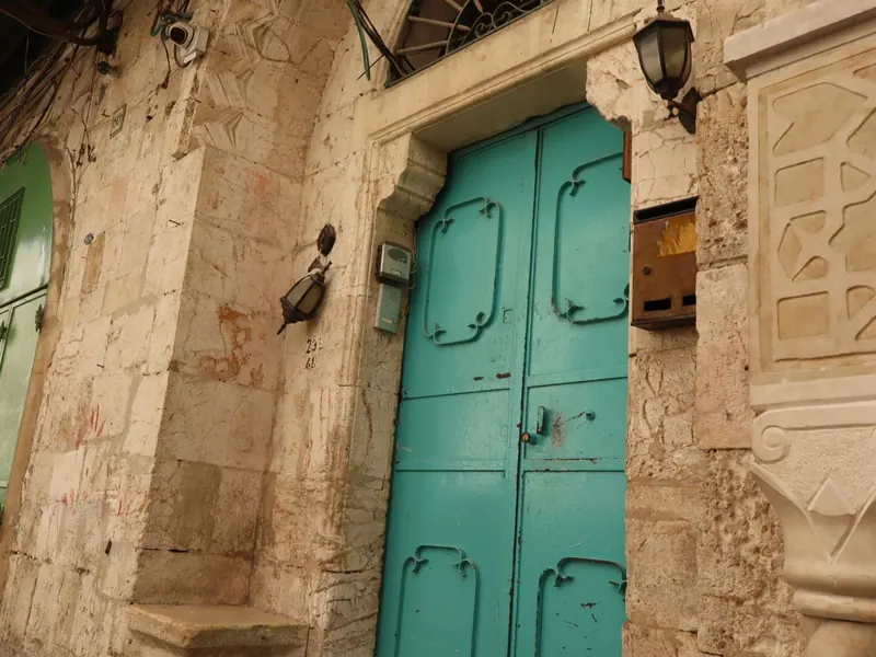 דלת ברזל בצבע טורקיז בקיר אבן, עם פנס קיר, תיבת דואר ואינטרקום.