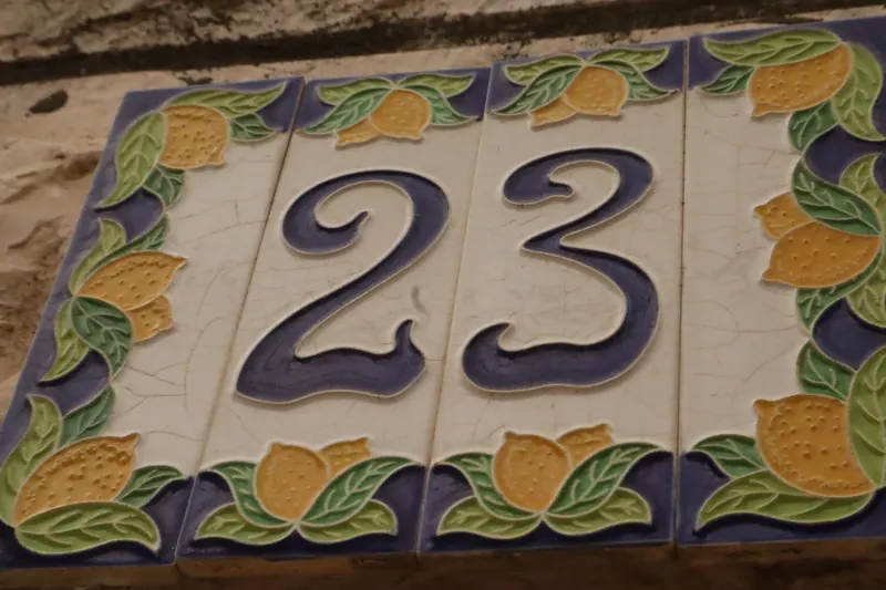 מספר בית 23 על אריחי קרמיקה מצוירים בלימונים ועלים, בקיר אבן.