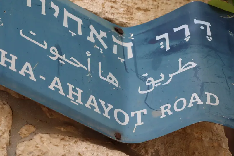 שלט רחוב כחול מעוקם על קיר אבן: "דרך האחיות" בעברית, בערבית ובאנגלית.