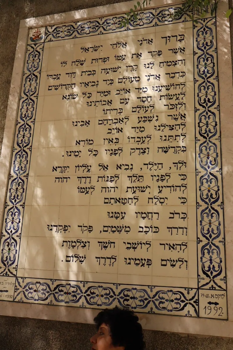 לוח אריחים עם תפילת "ברוך אדוני אלוהי ישראל" בעברית מנוקדת, לוקס א 79-68, 1992; ראשה של מבקרת בתחתית.