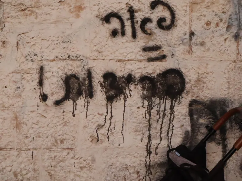 כתובת מרוססת בשחור על קיר אבן, מרוחה ונוזלת, ולידה ידית של עגלת ילדים.