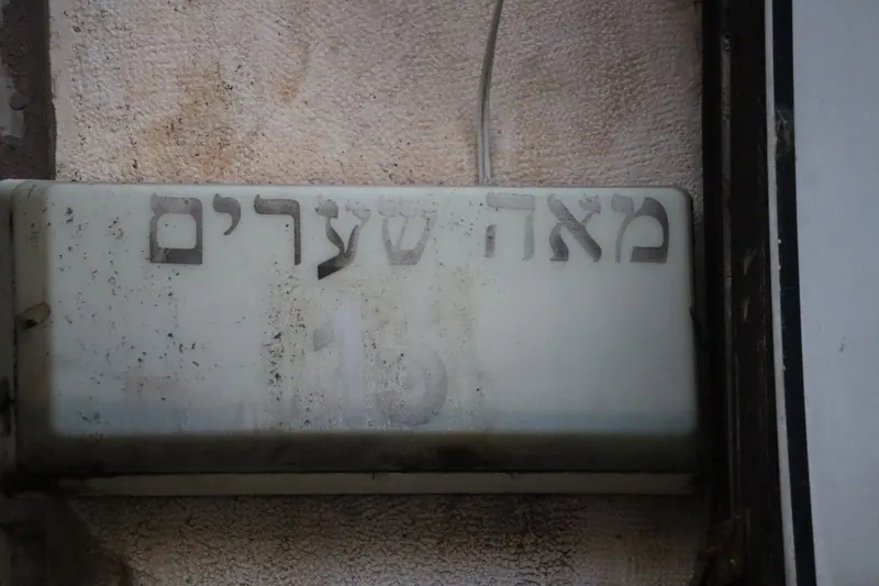 שלט אבן ישן ובלוי בקיר ועליו הכיתוב "מאה שערים".