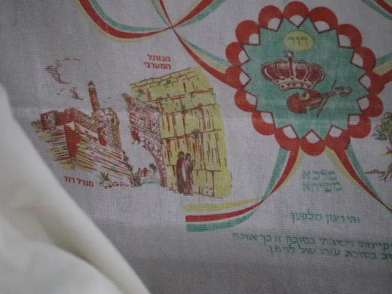 קישוט בד מודפס בסוכה: מגדל דוד, הכותל המערבי ומתפללים לידו, וכתר בתוך מגן מעוטר.