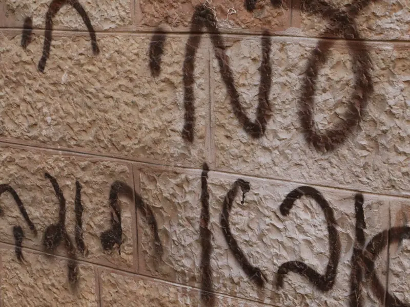 אותיות עבריות מרוססות בצבע חום כהה על קיר אבן מסותתת.