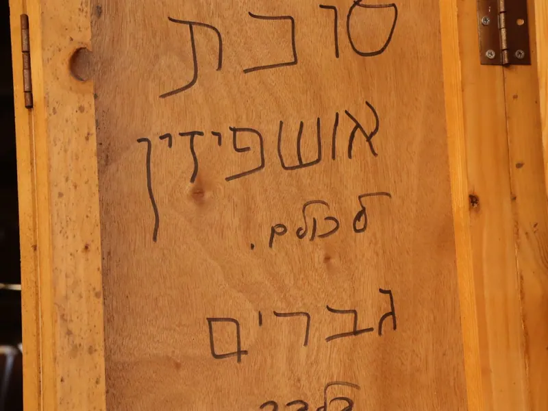 דופן סוכה מעץ ועליה כתוב בטוש: "סוכת אושפיזין לכולם. גברים".