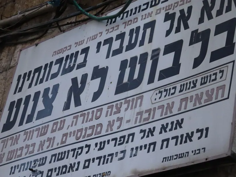 שלט מתכת ישן בין חוטי חשמל: "אנא אל תעברי בשכונתינו בלבוש לא צנוע", ומתחתיו "רבני השכונות".